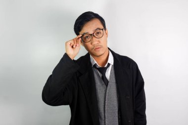 Asyalı bir adam mafya gibi giyinmiş, gözlük takıyor ve elinde gözlükle ciddi bir ifade takınıyor.