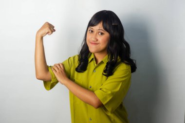 Yeşil tişört giyen kendine güvenen Asyalı bir kadın, korkunç bir ifadeyle, kas esnetici bir jest yapıyor.