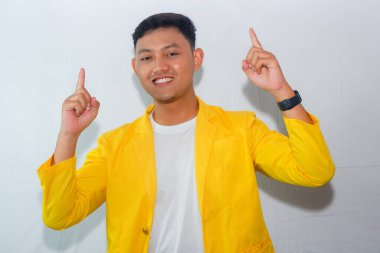 Dost canlısı, sarı takım elbiseli genç Asyalı adam yukarı doğru hareketler yapıyor.