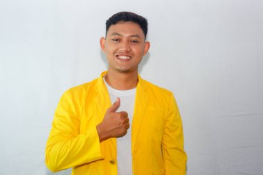Sarı takım elbiseli genç Asyalı adam baş parmak hareketi yapıyor.