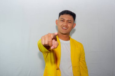 Sarı takım elbiseli kendinden emin genç Asyalı adam kameraya işaret ediyor.