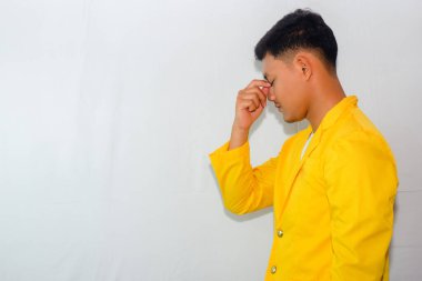 Sarı takım elbiseli genç Asyalı bir adam baş ağrısı çekiyor. Bir şey düşünüyor.