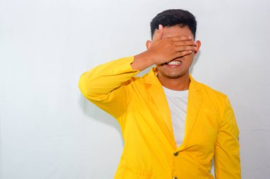 Sarı takım elbiseli genç Asyalı gözlerini ve yüzünü buruşturuyor.