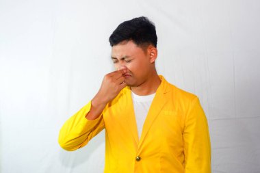 Kokudan dolayı sarı takım elbiseli genç Asyalı adam burnunu kapatıyor.