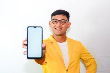 Sarı takım elbiseli ve gözlüklü genç Endonezyalı adam, boş akıllı telefon ekranı gösteriyor.