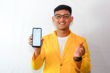 Endonezyalı genç adam sarı takım elbiseli ve gözlüklü, akıllı telefon boş ekranı gösteriyor ve sarangheo hareketi yapıyor.
