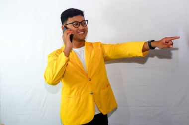 Sarı ceketli ve gözlüklü genç Endonezyalı adam telefonla konuşuyor.