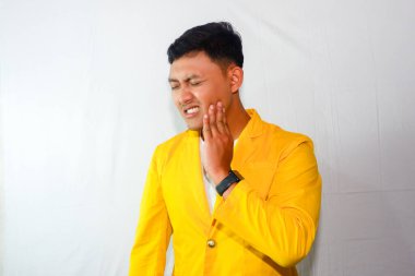 pria muda asia memakai jas kuning kesakitan karena sakit gigi