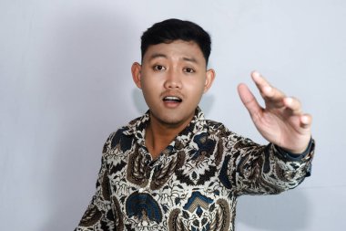 Batik giyen genç Endonezyalı bir adam selamlama ya da hoş geldin jesti yapıyor.