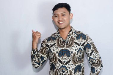 Batik giyen genç Endonezyalı adam baş parmaklarıyla kenarı işaret ediyor.