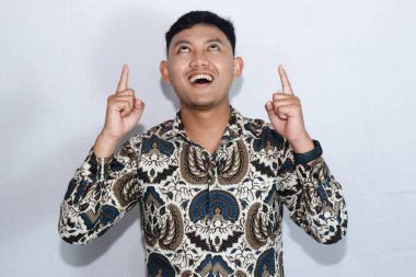 Gülümseyen yüzlü, batik takan, iki işaret parmağıyla işaret eden Endonezyalı genç adam.