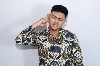 Batik giyen genç Endonezyalı adamın kulağı ağrıyor ve rahatsız.