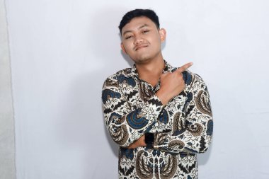 Genç Endonezyalı, şaşkın suratlı, batik giyen, işaret işareti yapan bir adam.