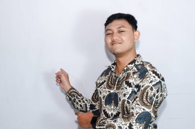 Şaşkın suratlı, batik giyen Endonezyalı genç adam iki işaret parmağıyla geriye doğru bir hareket yapıyor.