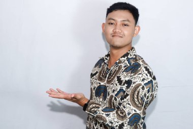 Dost canlısı genç Endonezyalı gülen yüzlü, batik giyinmiş ürünleri gösteren jestler yapan adam.
