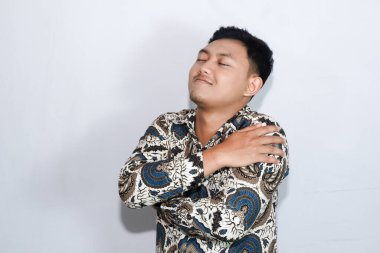 Mutlu genç Endonezyalı sakin yüzlü, batik giyinmiş, kendini beğenmiş hareketler yapan adam.