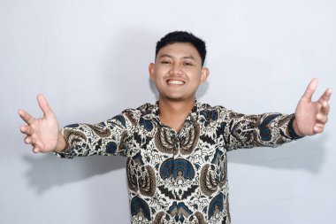 Mutlu, genç Endonezyalı sakin, batik giymiş bir adam selamlama ya da sarılma hareketi yapıyor.