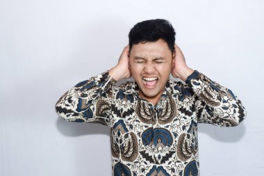 Batik giyen genç Endonezyalı adam kulaklarını kapatma hareketi yapıyor.