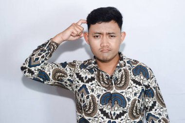 Batik giyen genç Endonezyalı bir adam düşünüyor ya da kafası karışık bir hareket yapıyor.