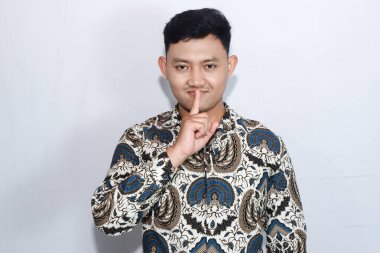 Batik giyen genç Endonezyalı adam ağzını kapatması için bir jest yapıyor.