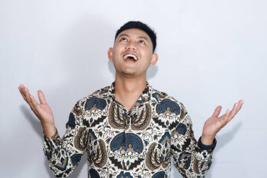 Batik giyen Endonezyalı genç adam elleriyle yukarı bakıyor.