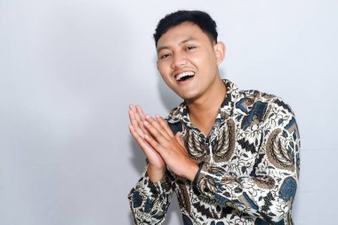 Genç Endonezyalı gülen yüzlü batik giyen adam alkışlıyor.