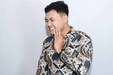 Genç Endonezyalı adam diş ağrısı yüzünden yüzü ağrıyan batik takıyor.