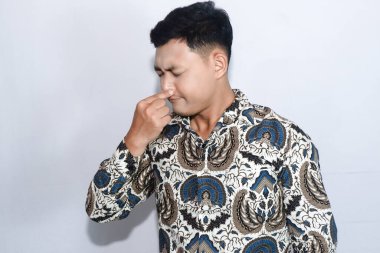 Batik giyen genç Endonezyalı adam koku yüzünden burnunu kapatıyor.