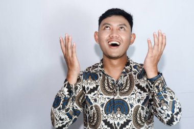 Genç Endonezyalı gülen yüzlü Batik giyen adam Tanrı 'ya şükranlarını sunuyor.