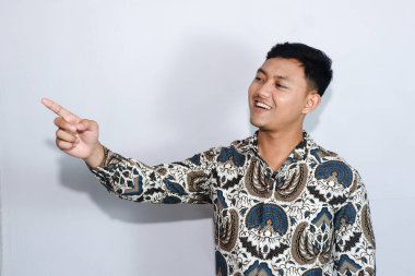 Genç Endonezyalı batik giyen sakin yüzlü adam yan tarafı işaret ediyor.