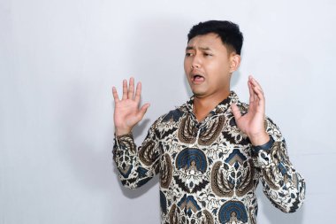 Genç Endonezyalı adam şaşkınlıktan şaşkın bir ifadeyle batik takıyor.