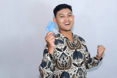 Genç Endonezyalı gülen yüzlü adam kredi kartı gösteriyor ve başarıyı kutluyor.