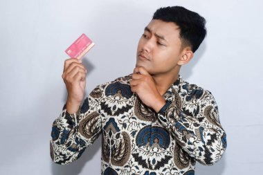 Genç Endonezyalı gülen yüzlü adam kredi kartını gösteriyor ve kredi kartına bakıyor.