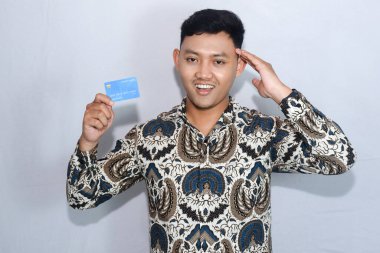 Genç Endonezyalı batik giyen, şaşırmış yüzlü, kredi kartı gösteren bir adam.