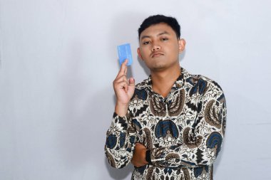 Genç Endonezyalı Batik giyen, yüzü çıkmış, kredi kartı ve kolları çaprazlanmış.