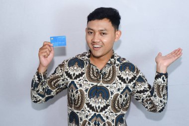 Genç Endonezyalı batik giyen, yüzü çıkmış, kredi kartı ve eli yan tarafı gösteren bir adam.