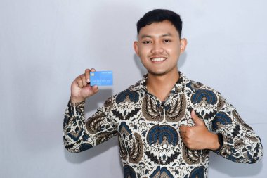 Genç Endonezyalı batik giyen, dost yüzlü kredi kartı gösteren ve onay veren bir adam.