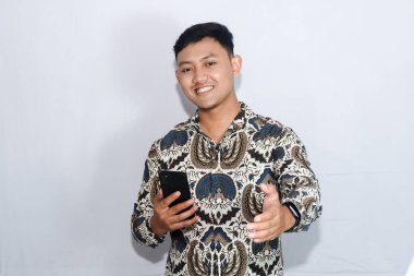 Genç Endonezyalı Batik marka cep telefonu takan heyecanlı yüzüyle davetkar bir jest yapıyor.