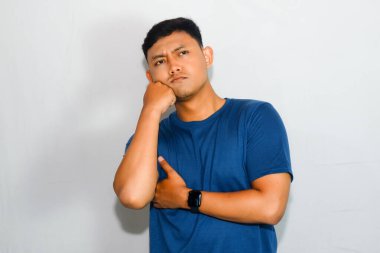 Asyalı adam mavi gömlekli, bir şey düşünüyor ya da hayal ediyor.