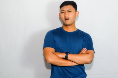 Asyalı adam mavi gömlekli, kolları çapraz, şaşırmış yüzlü.