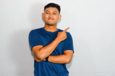 Mavi tişörtlü genç Asyalı sakin bir yüzle yan tarafı gösteriyor.