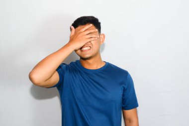 Mavi tişörtlü genç Asyalı adam göz kapama hareketi yapıyor.