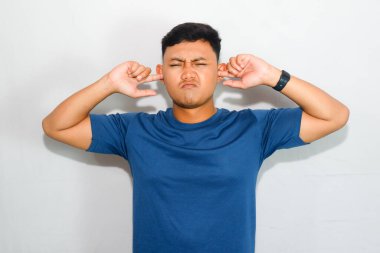 Mavi tişörtlü genç Asyalı adam kulak kapatma hareketi yapıyor.