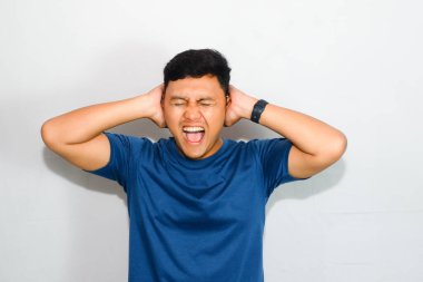 Mavi tişörtlü genç Asyalı adam kulak kapatma hareketi yapıyor.