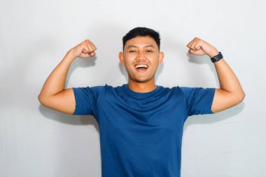 Mavi tişörtlü genç Asyalı adam kas hareketi yapıyor.