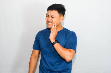 Dişi ağrıdığı için yüzünde rahatsız edici bir ifade olan mavi tişörtlü genç Asyalı.