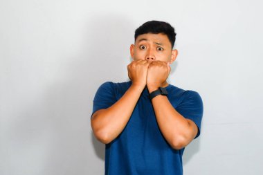 Mavi tişörtlü genç Asyalı adam korku dolu bir ifadeyle parmak ısırma hareketi yapıyor.