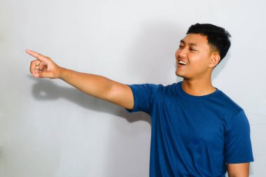 Tişörtlü arkadaş canlısı Asyalı genç adam, yan tarafı işaret ediyor.