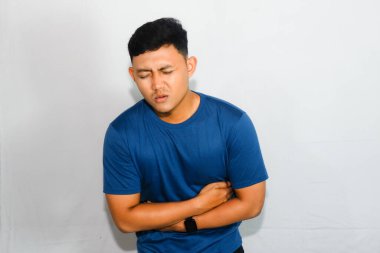 Mavi tişörtlü, midesi ağrıyan genç Asyalı adam.