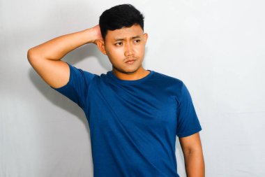 Mavi tişörtlü genç Asyalı adam, kafası karışık bir ifade takınıyor.
